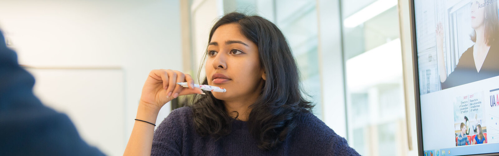 horizontal image of woman holding a pen and thinking