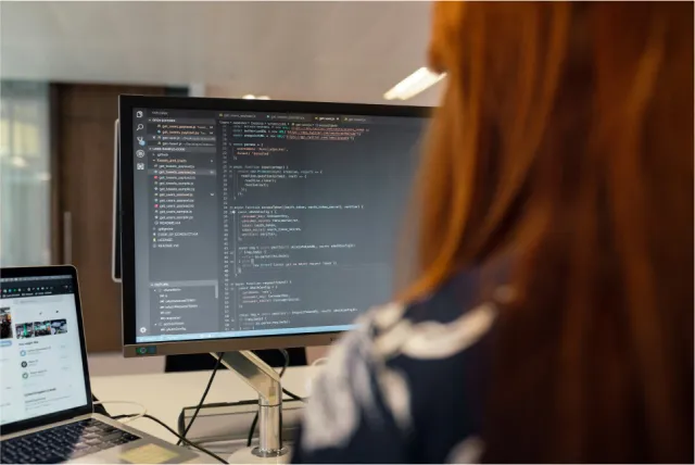A person working on code displayed on a large monitor.