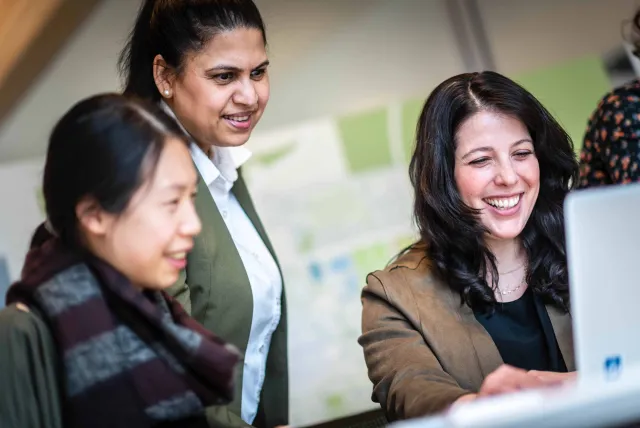 Three colleagues smiling and looking at a laptop together.