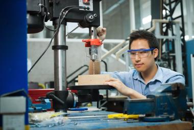 A man with safety glasses on using drilling equipment on the table.