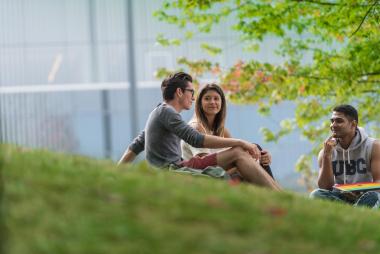 three students sitting on a grass hill chatting.