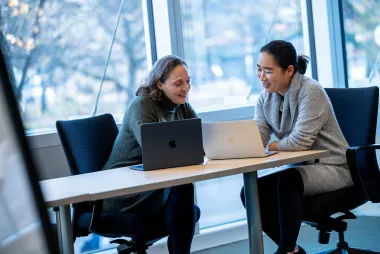 two women looking at each others laptops.